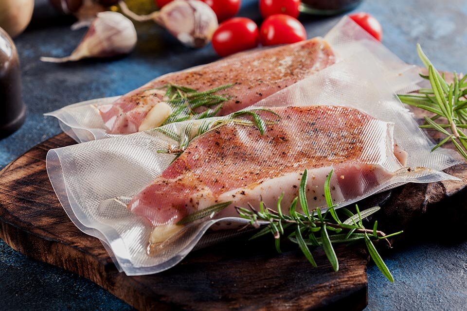 Zdjęcie mięsa w towarzystwie ziół i przypraw, umieszczonego w woreczku próżniowym, ilustruje pieczenie metodą air sous vide